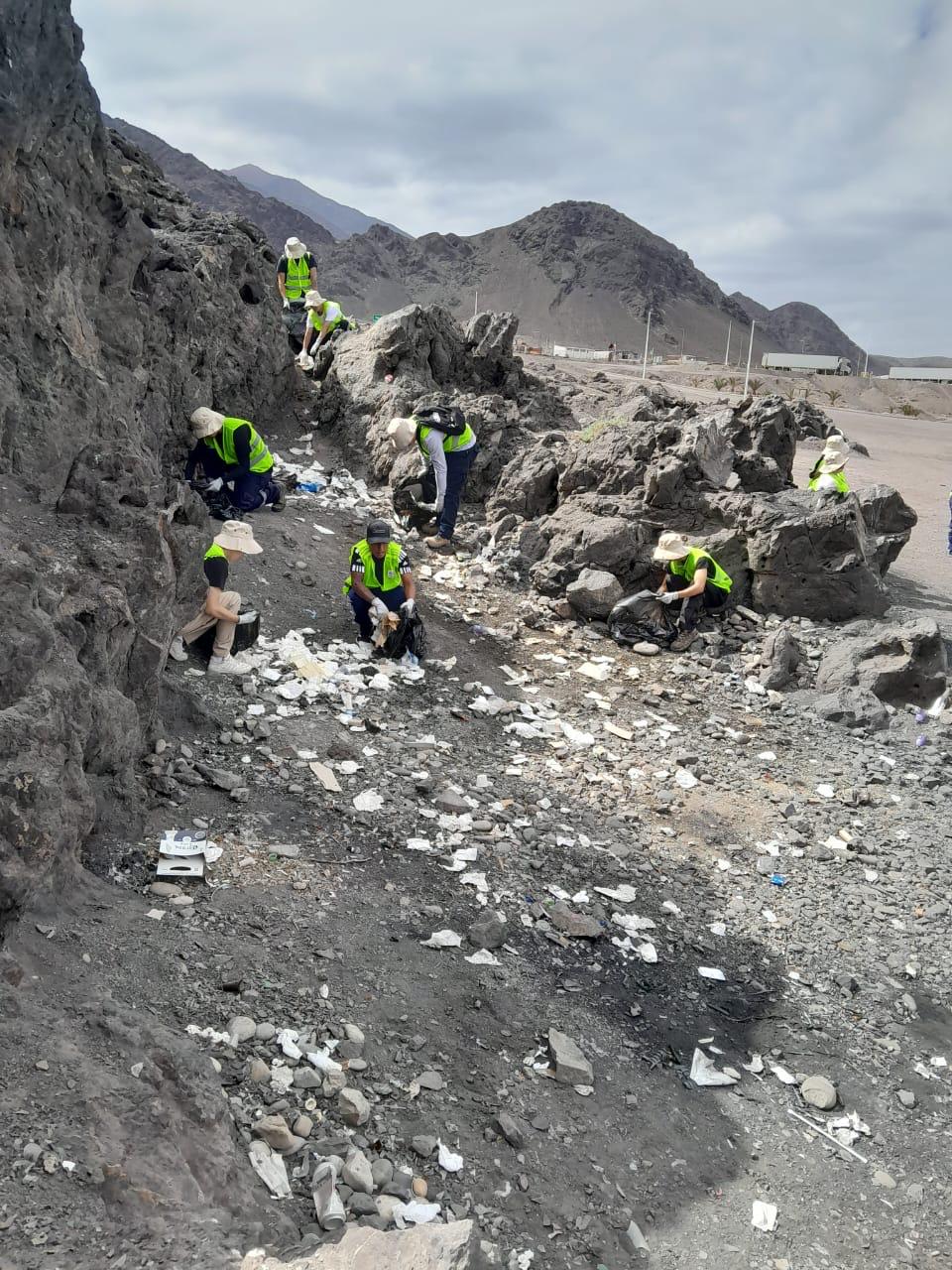 Equipo del Team Verano Taltal realiza limpieza y retiro de residuos entre roqueríos, usando chalecos reflectantes y bolsas de basura.