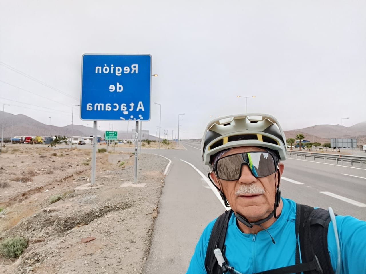 Pedro Lemus posa junto a un cartel de “Región de Atacama” en plena carretera, avanzando en su travesía en bicicleta.