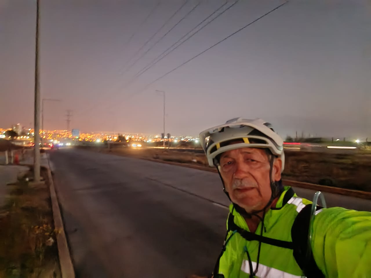 Pedro Lemus en un tramo nocturno de carretera, con luces de ciudad al fondo, durante su viaje en bicicleta hacia Taltal.