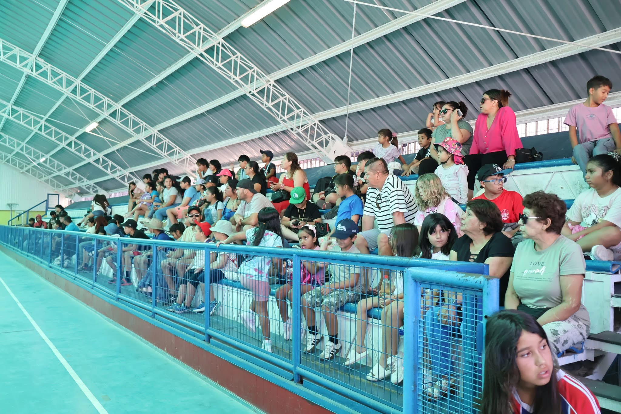 Padres y apoderados sentados en las graderías acompañando a sus hijos en el inicio oficial de la Escuela de Verano.