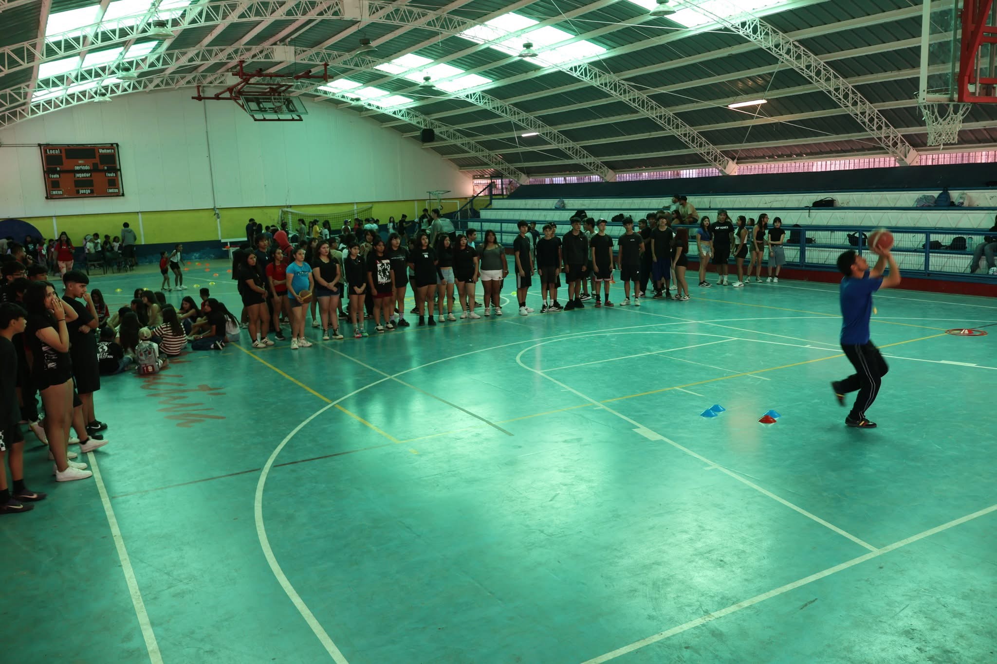 Un joven practicando lanzamientos de básquetbol bajo la atenta mirada de sus compañeros en el Estadio Techado de Taltal.