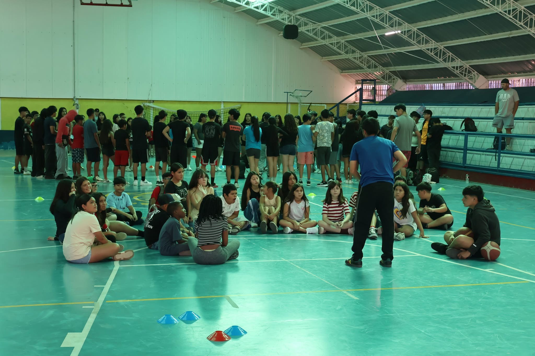 Niños y jóvenes sentados en círculo en el Estadio Techado participando en dinámicas de grupo y sana convivencia.