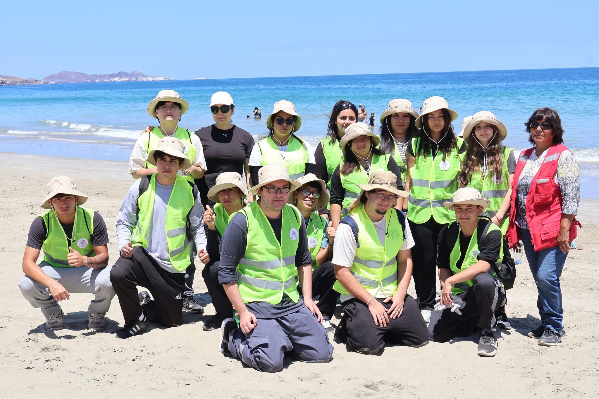 Grupo de jóvenes del Team Verano posando en la arena de Playa Tierra del Moro con sus uniformes institucionales.