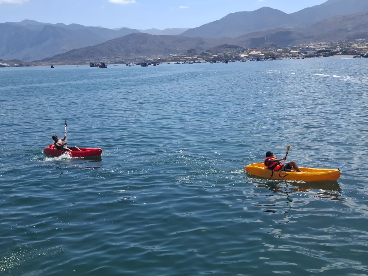 Dos niños remando en kayaks individuales color rojo y amarillo en el mar.