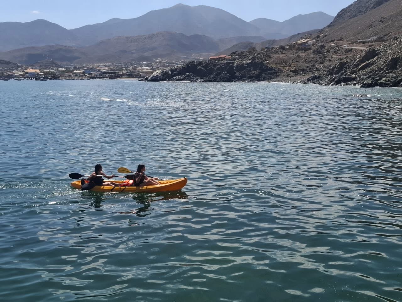 Dos niñas remando coordinadas en un kayak doble amarillo en el mar.