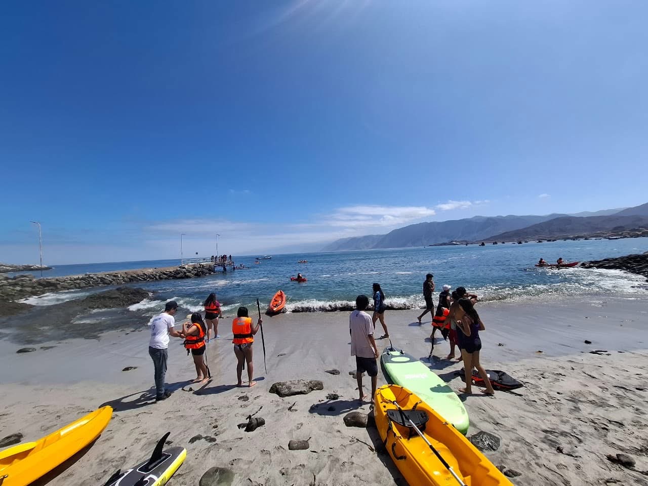 Equipos de kayak y alumnos preparándose para la actividad náutica en la arena.