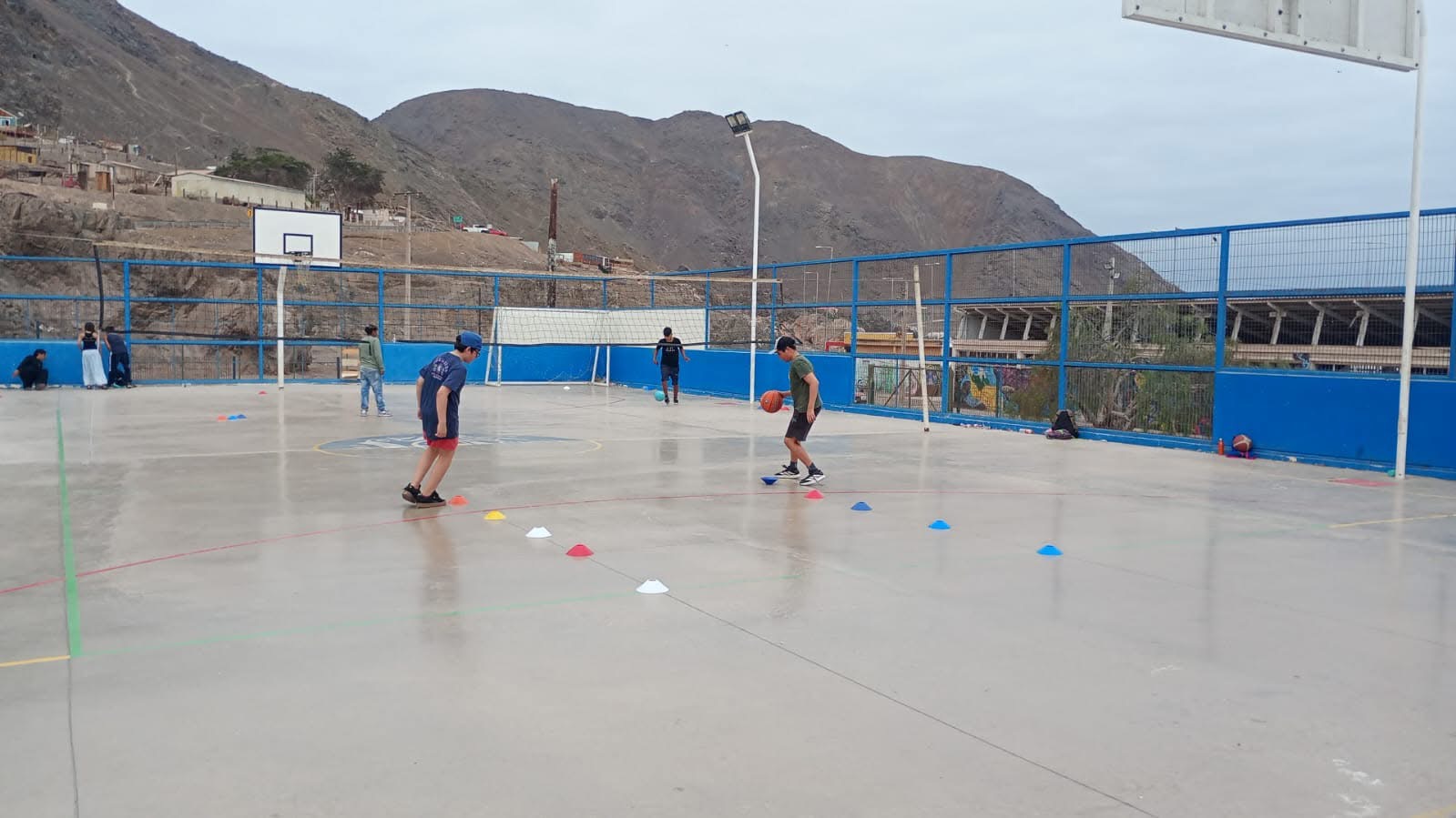 Niño practicando drible entre conos en cancha exterior de básquetbol.