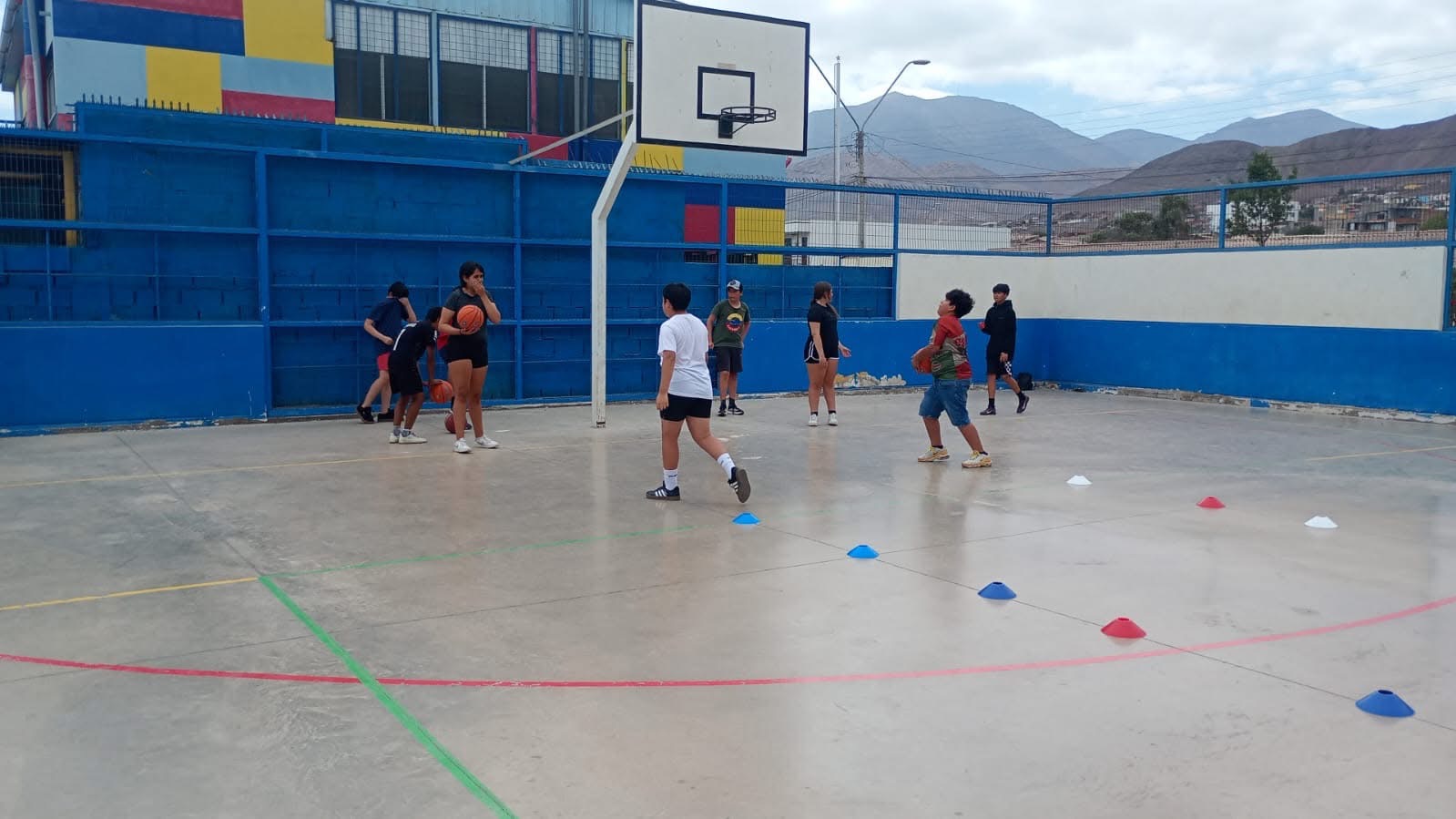 Niños practicando técnicas de tiro y drible en cancha exterior azul.