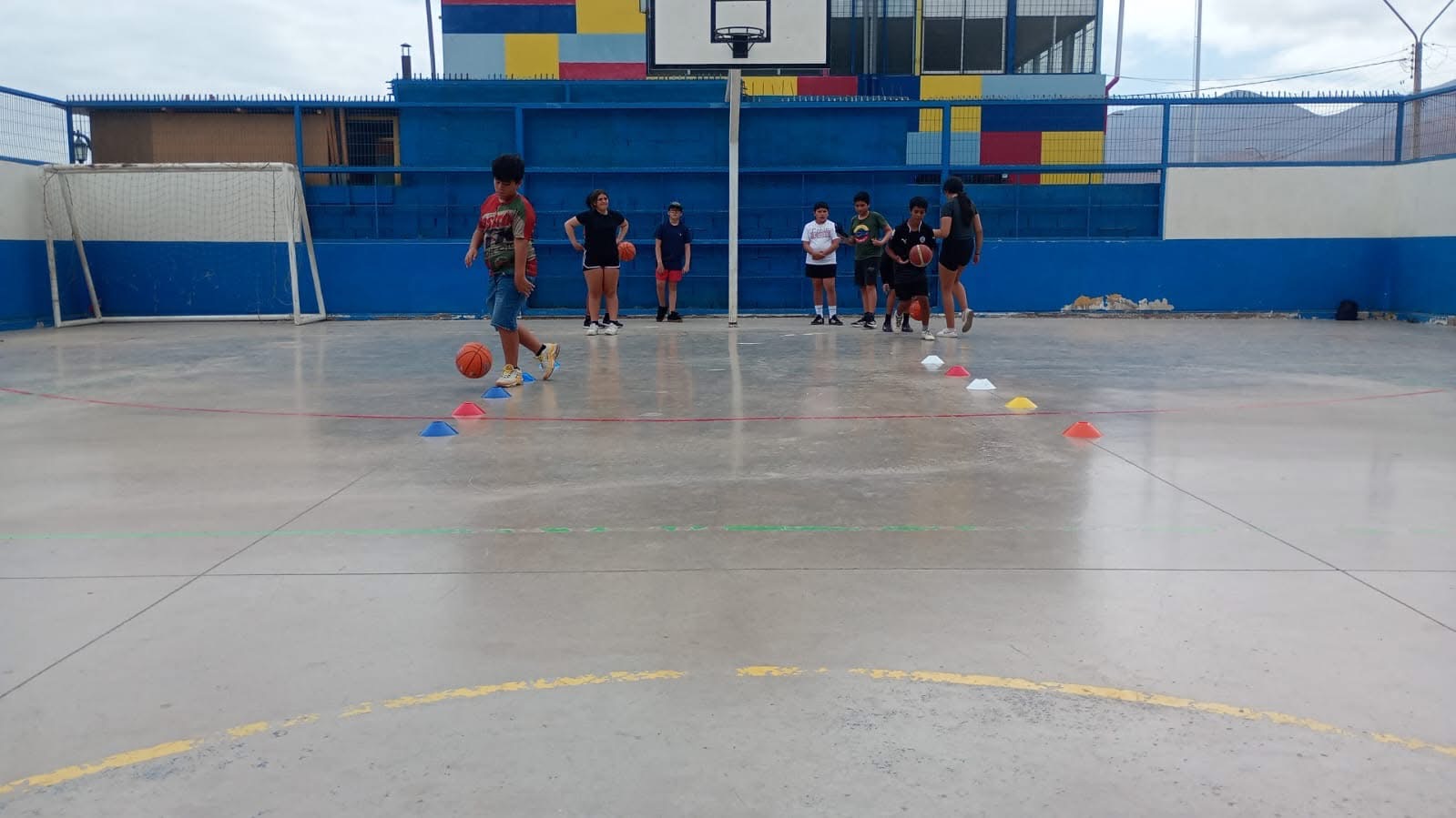 Niño en circuito de entrenamiento con balón de básquetbol en cancha abierta.