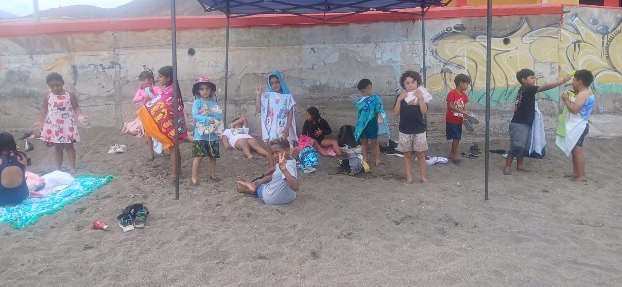 Niños de la escuela de verano descansando bajo un toldo en la playa.