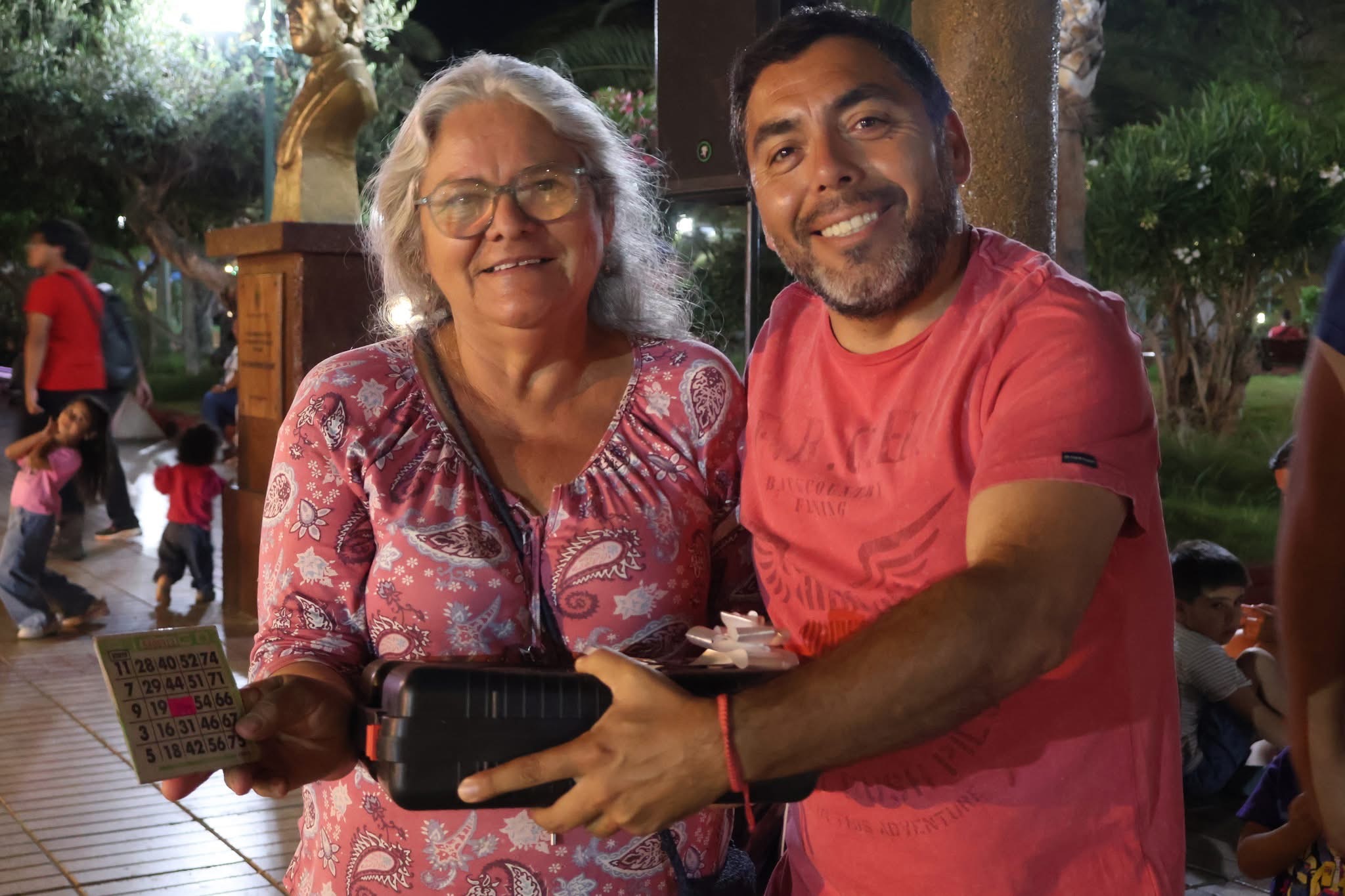 Vecinos mostrando su cartón ganador y el premio obtenido en la jornada estival.