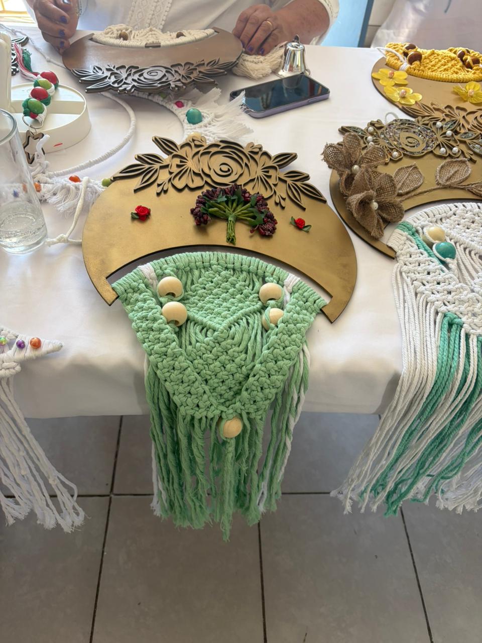 Espejo circular decorado con flecos verdes de macramé y aplicaciones de flores de madera.