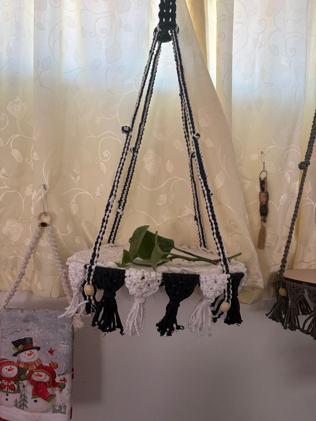 Repisa colgante tejida en blanco y negro, ideal para plantas o decoración de interiores.