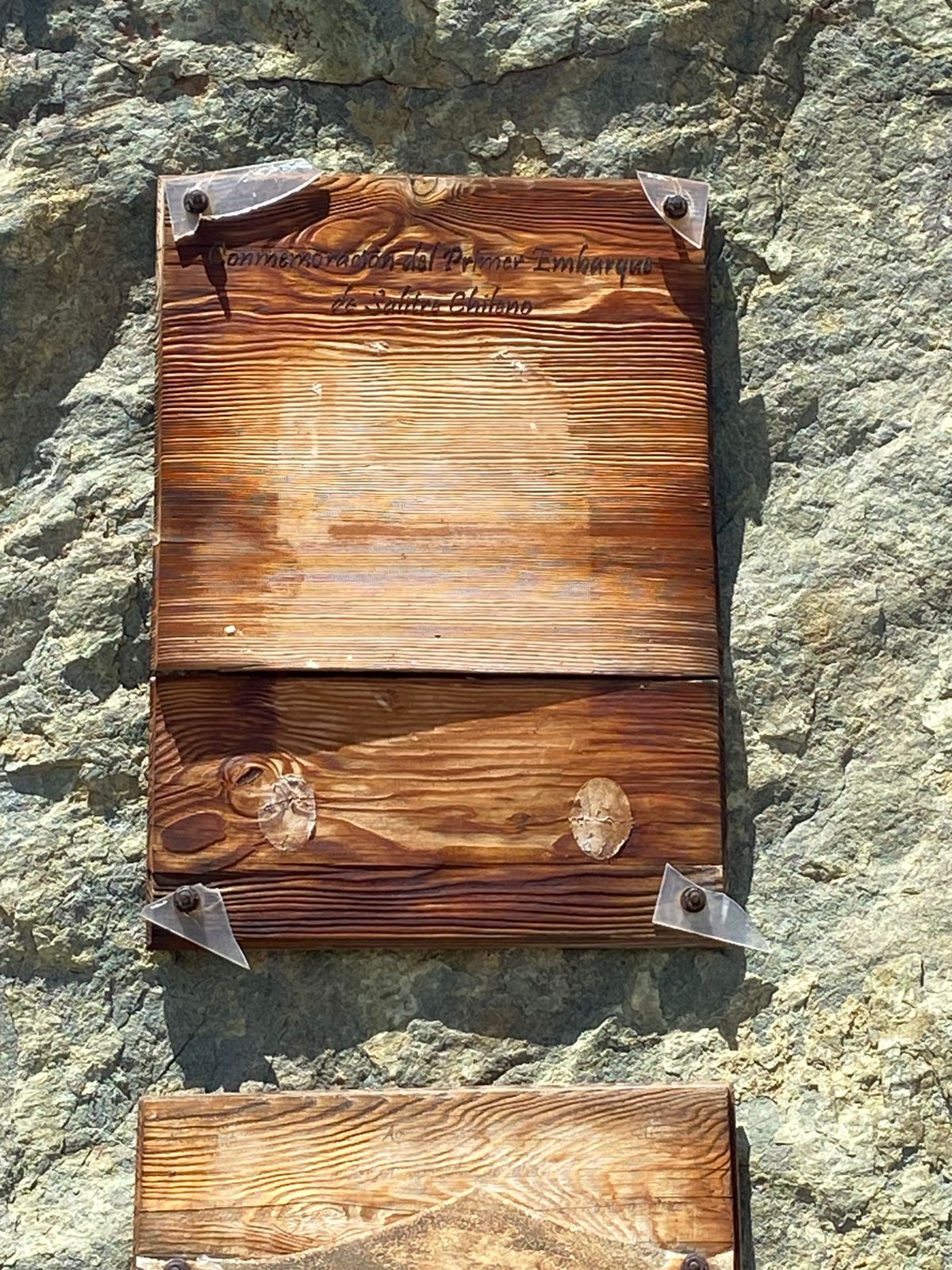 Placa de madera instalada en las rocas de Puerto Oliva conmemorando el primer embarque de salitre netamente chileno.