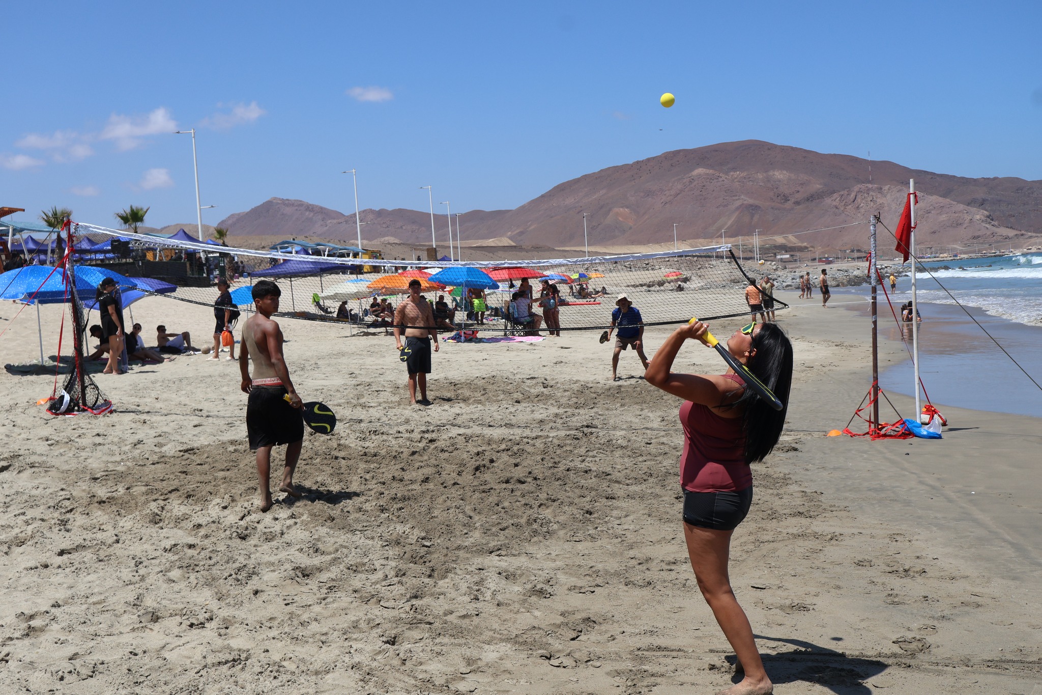 Juego de tenis playa en Tierra del Moro con público y quitasoles al fondo durante jornada de verano en Taltal.