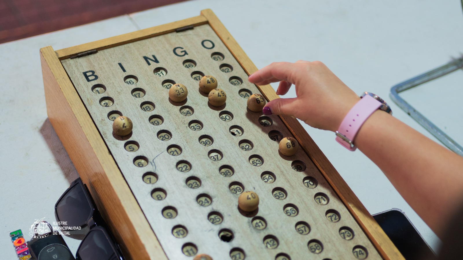 Tablero de bingo con números marcados con maíz y cartones cercanos durante ronda del Gran Bingo Veraniego en Plaza Prat, Taltal. Jornada del programa Taltal en Movimiento – Verano 2026.