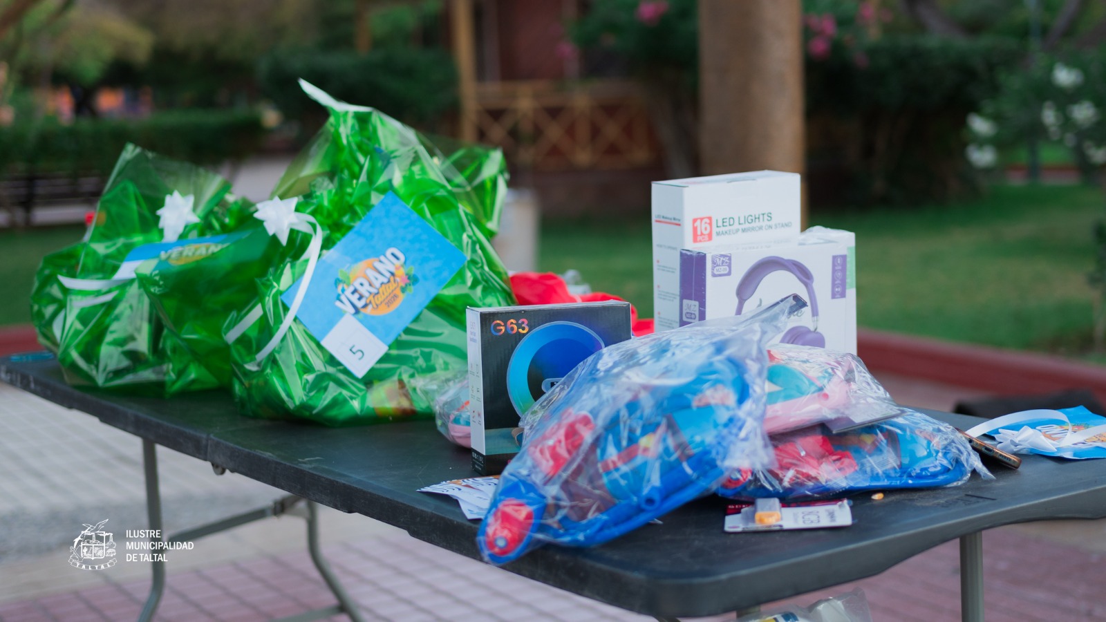 Mesa con regalos y bolsas Veranando 2026, incluyendo audífonos, luces LED y juguetes, durante la tercera jornada del Gran Bingo Veraniego en Plaza Prat, Taltal, enero-febrero 2026.