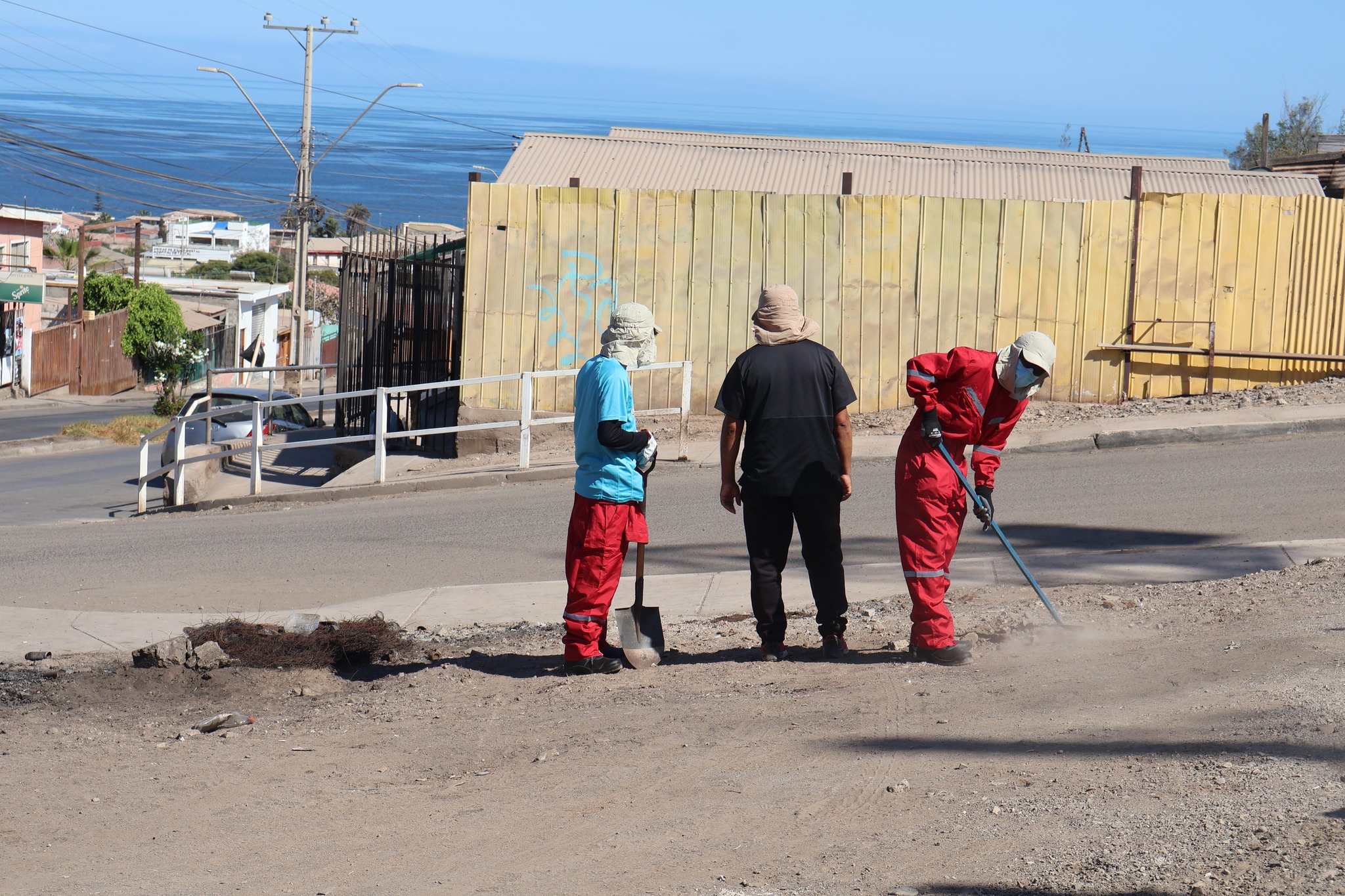 Miembro del Team Verano 2026 nivelando terreno con rastrillo en Pasaje Entel, Taltal, como parte de las acciones de limpieza y creación de áreas verdes en jornada municipal, enero 2026.