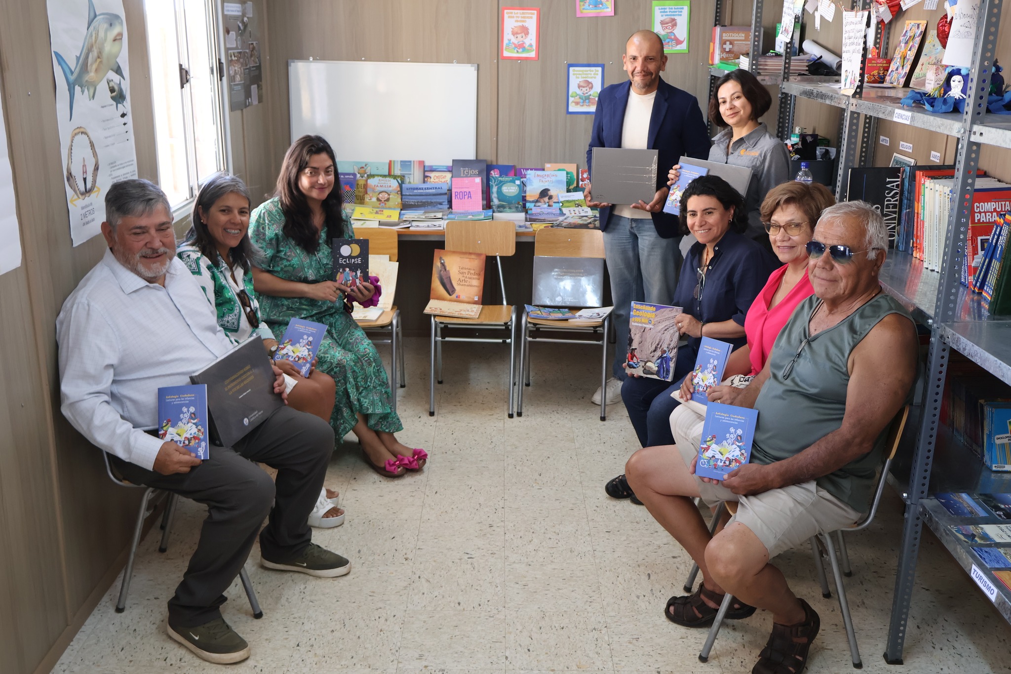 Participantes posan en el interior de la biblioteca con libros donados para fortalecer la colección de Caleta Cifuncho.