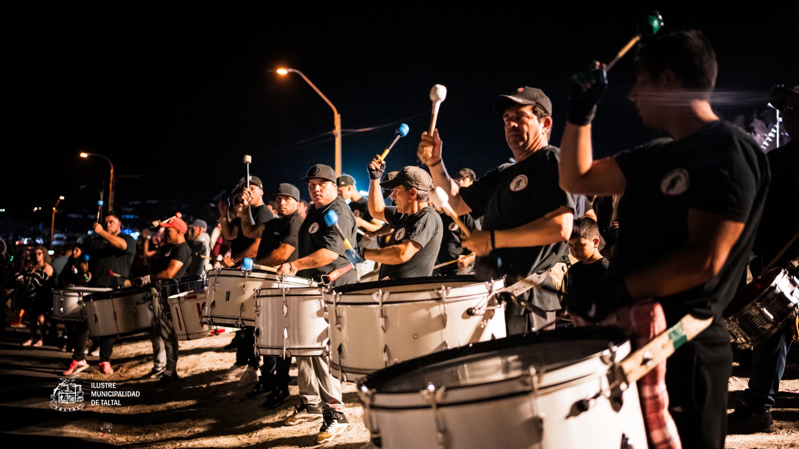 Percusionistas adultos tocando tambores y mazas en fila durante procesión Fiesta Virgen de Lourdes sector La Puntilla Taltal 2026