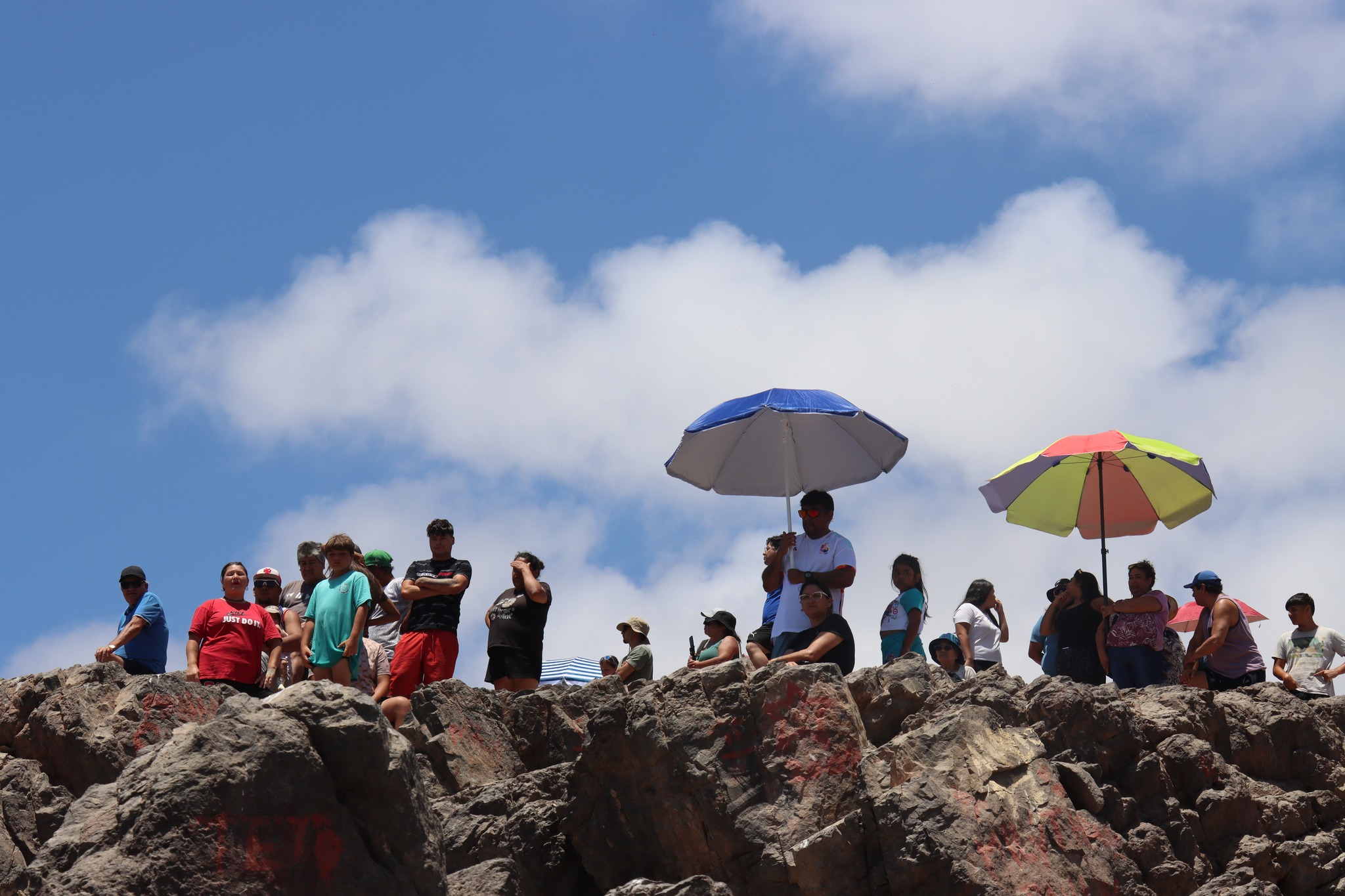 Multitud en mirador rocoso con sombrillas observando travesía a nado Tarzán Álvarez Virgen de Lourdes Taltal febrero 2026.