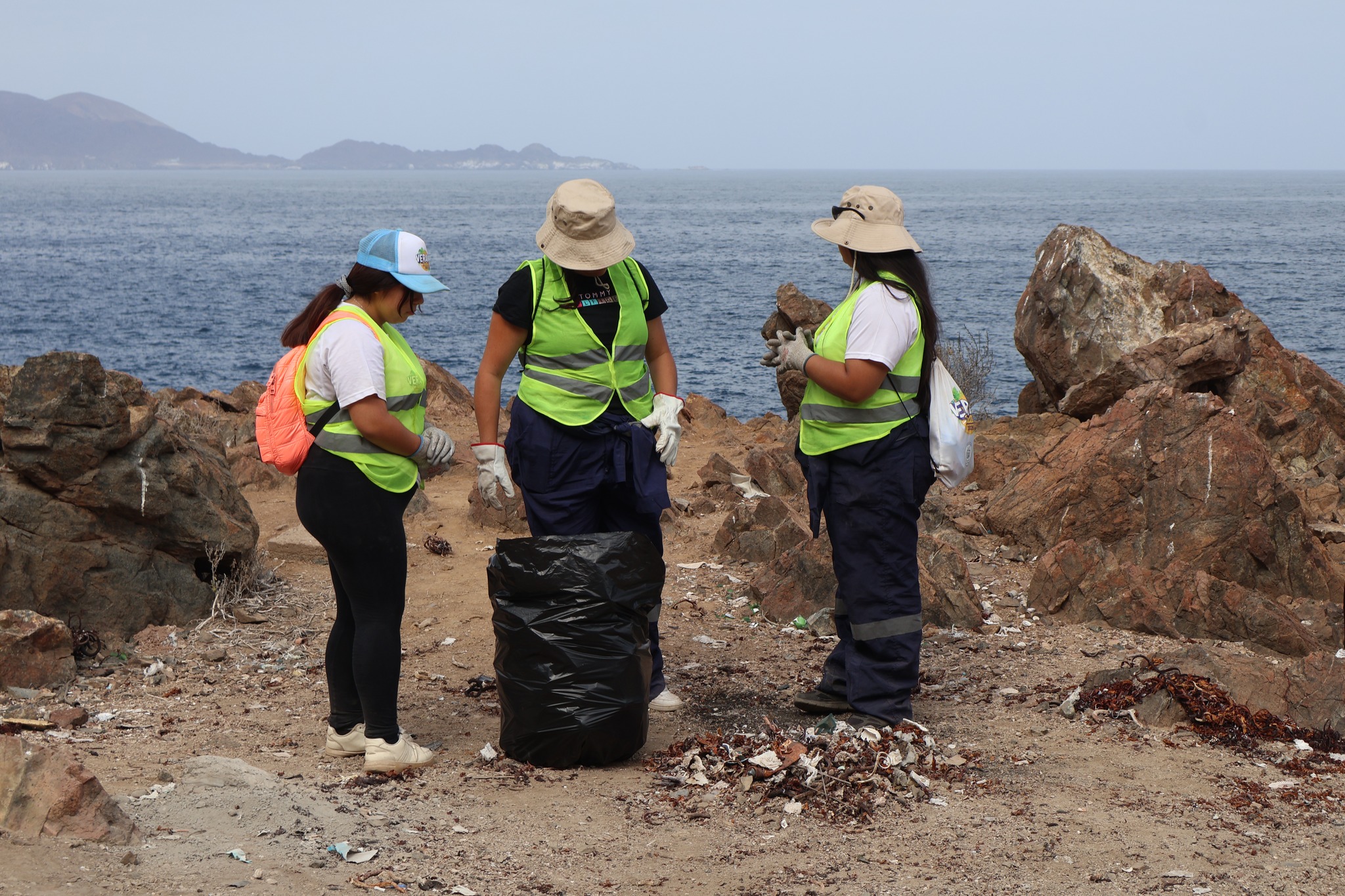 Equipo de Team Verano 2026 coordina labores de limpieza en el Sitio Arqueológico Los Vientos, Taltal, con el mar de fondo y enfoque en protección patrimonial (febrero 2026).
