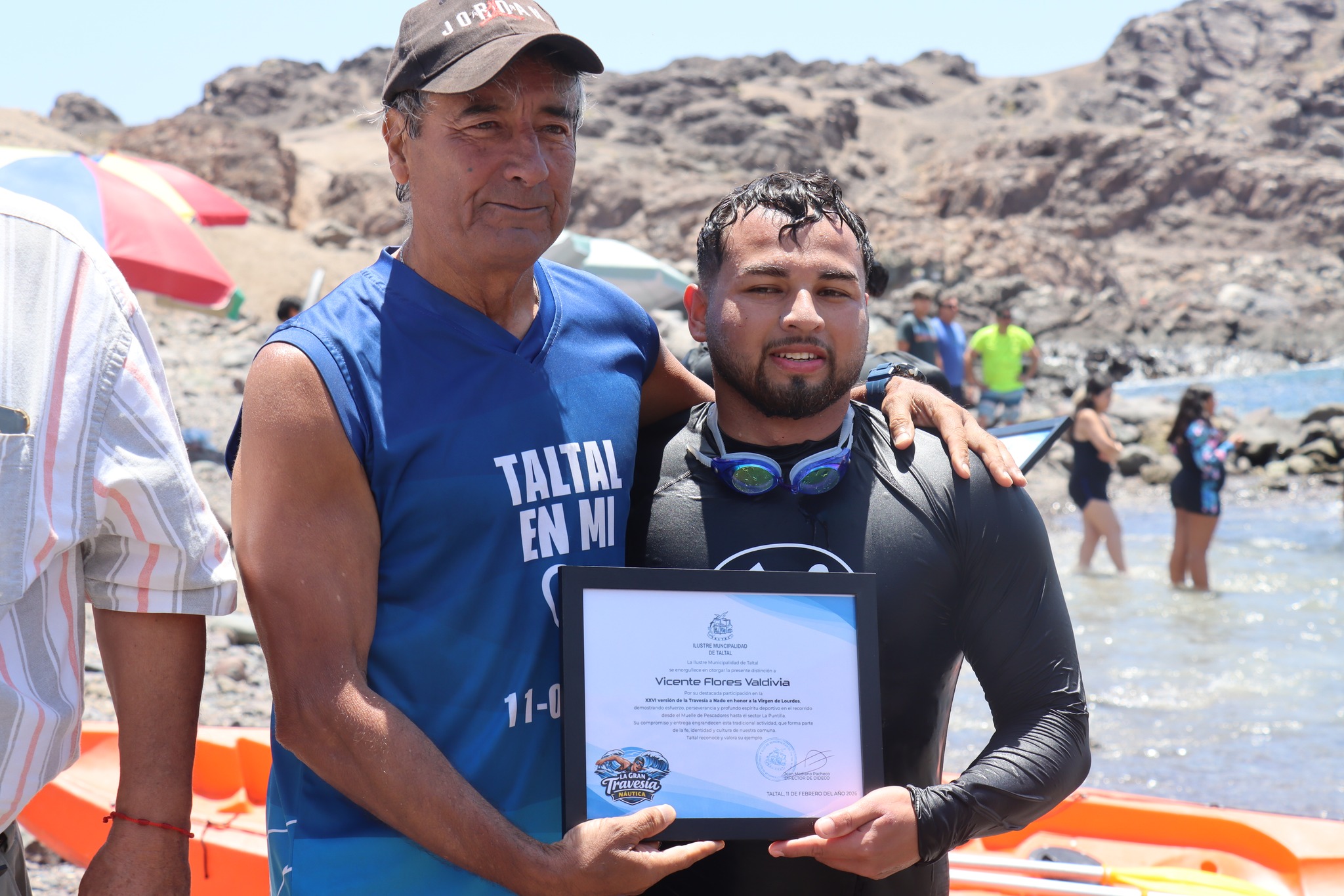 Tarzán Álvarez abraza a Vicente Flores Valdivia tras entrega de reconocimiento por participación en 26° travesía Virgen de Lourdes Taltal febrero 2026.