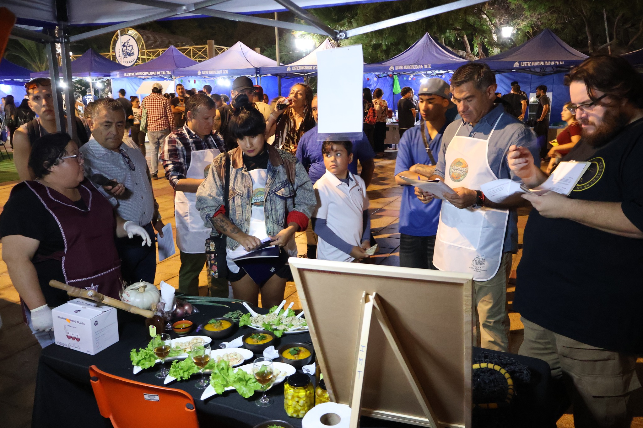 Jurado del concurso “Sabores Marinos” evalúa preparación en stand gastronómico, Plaza/Paseo peatonal de Taltal, verano 2026.