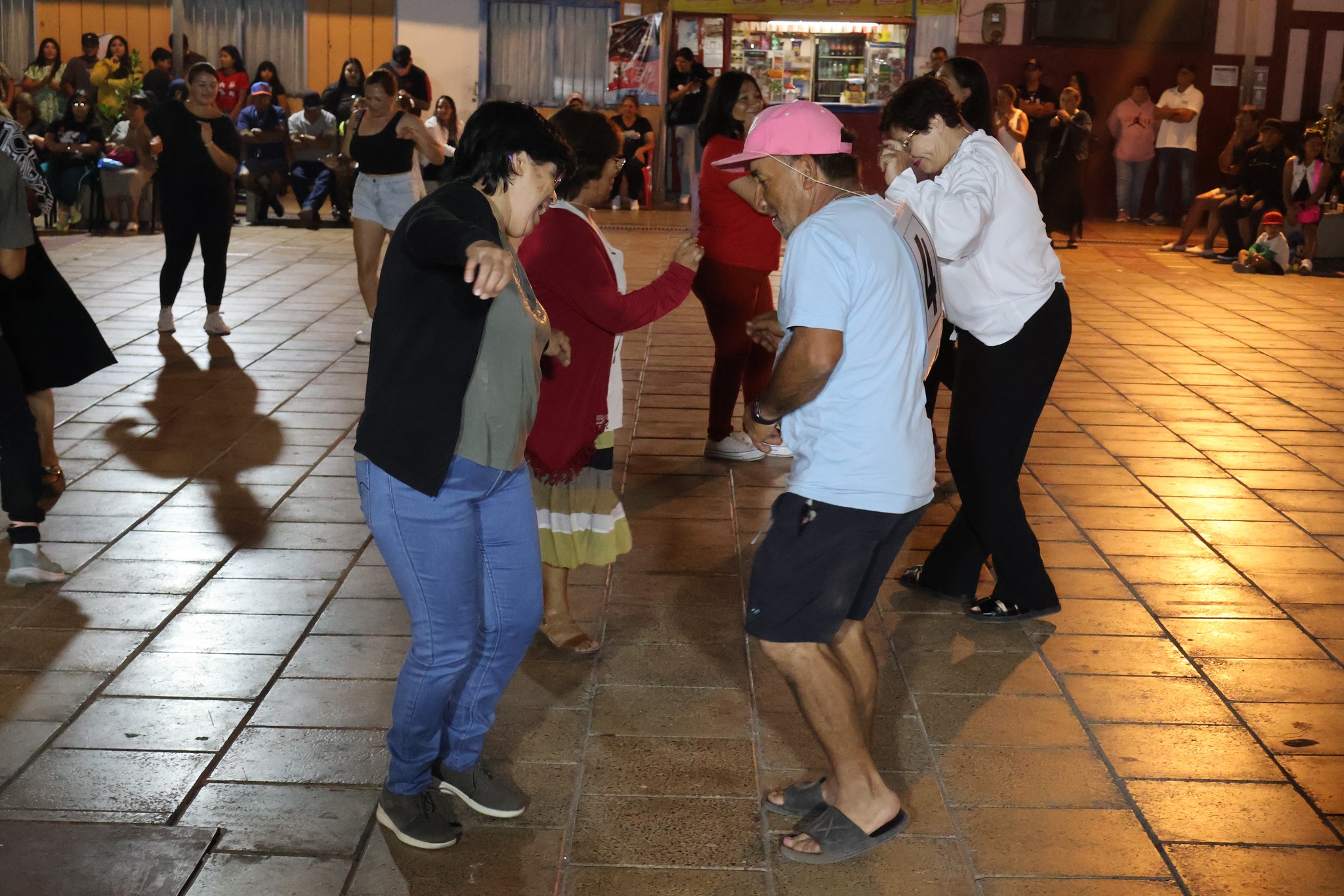 Participantes adultos bailan en ronda frente al público durante la actividad.