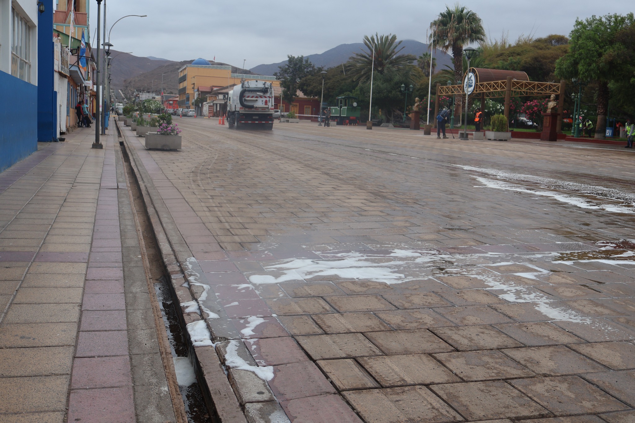 Vista general del operativo de limpieza de Plaza Prat con camión municipal y personal del Departamento de Aseo y Ornato de la Municipalidad de Taltal.