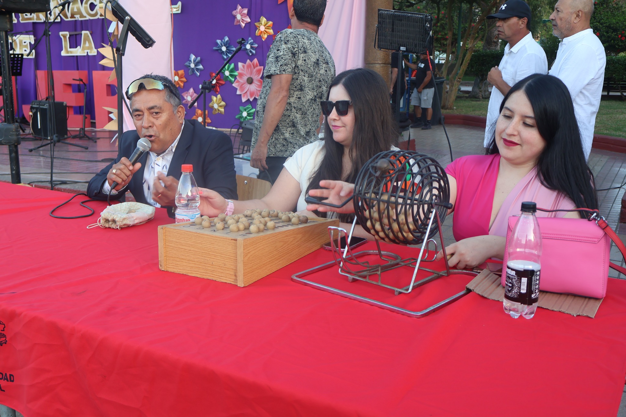 Locutor anima bingo con tómbola y participantes en Plaza de Armas durante actividad del Día de la Mujer en Taltal.