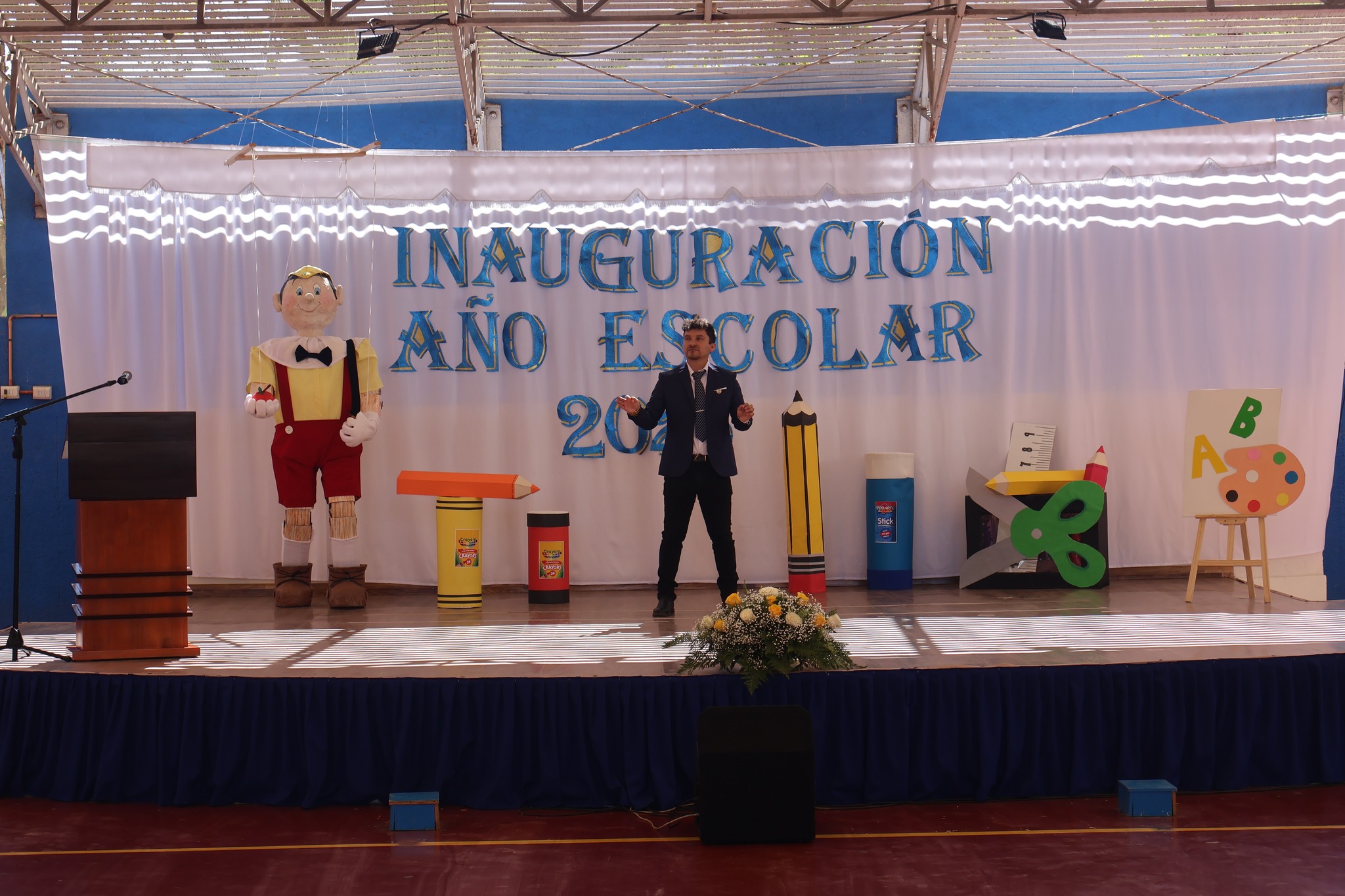 Profesor Sebastián Vilalobos dirigiendo el hiimno nacional en el escenario principal durante la ceremonia de inauguración del Año Escolar 2026 en la Escuela Alondra Rojas Barrios de Taltal.